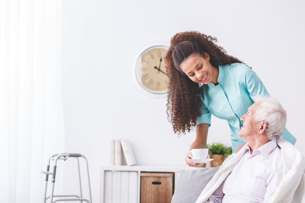 Auxiliaire de vie servant une tasse de thé à un homme âgé dans son salon