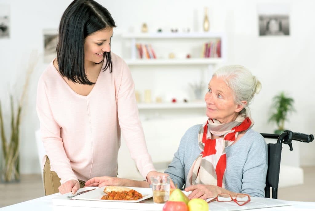 Jeune femme apportant un repas à une femme âgée en fauteuil roulant à domicile