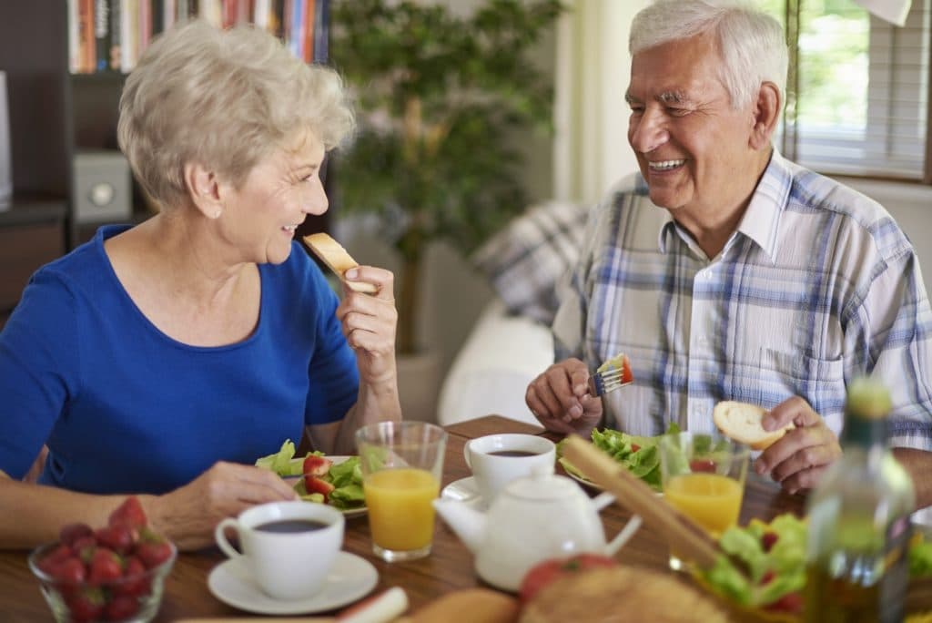 Couple âgé partageant un repas à domicile, sourires et convivialité